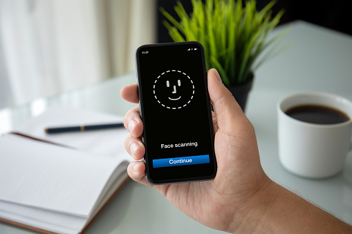 male hand holding phone with face ID scanning on screen in the office