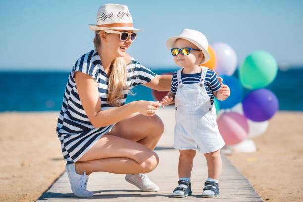 幸せなママと小さな息子は晴れた日に青い海の近くの日当たりの良いビーチで一緒に楽しんでいます - child balloon outdoors little boys ストックフォトと画像
