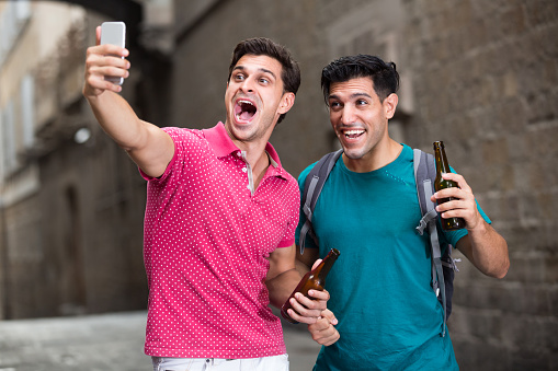 Two male fans are drinking beer and making selfie on smarphone after football match in Barcelona.