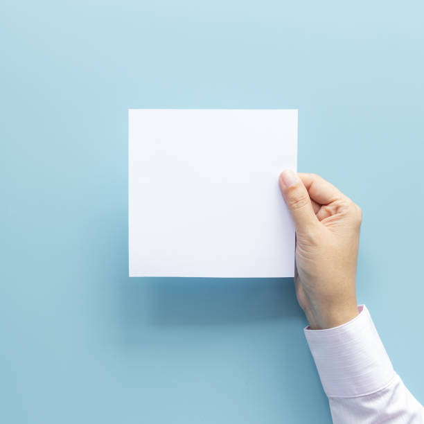 istock woman hand holding blank paper sheet isolated on blue background with copy space. 1175652171