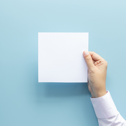 woman hand holding blank paper sheet isolated on blue background with copy space.