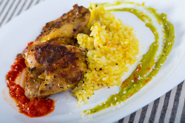 Tasty  chicken thighs with red and green sauces and rice at plate on table