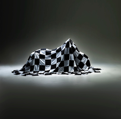 Prototype product hidden under black and white checkered cloth cover on studio background