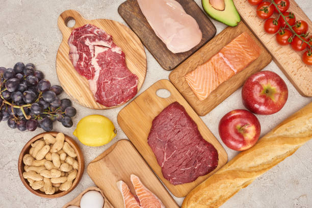 istock Top view af raw organic assorted meat, poultry, fish, apples, grape, lemon, avocado, tomatoes and peanuts on wooden cupboards with fresh baguette on marble surface 1175653821