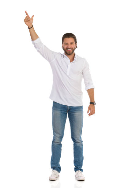 Smiling Handsome Young Man Is Standing With Arm Raised And Pointing Up stock photo
