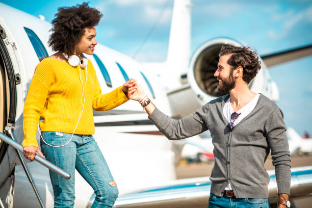 caballero rico sosteniendo la mano de su pareja mientras ella está saliendo de un avión privado estacionado - status symbol audio fotografías e imágenes de stock