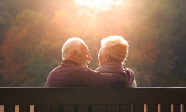 pareja mayor sentada en el banco en el parque de otoño - autumn women park forest fotografías e imágenes de stock