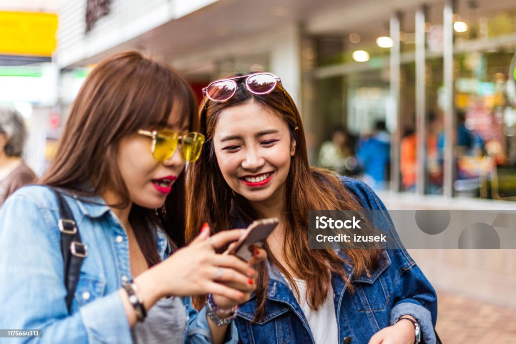 Young woman showing smart phone to friend in city Young woman showing smart phone to friend. Females are spending leisure time in city. They are wearing casuals. 20-24 Years Stock Photo
