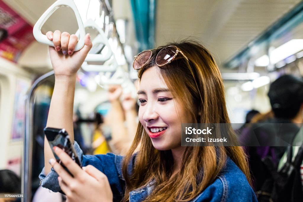 Close-up of smiling woman using smart phone Close-up of smiling woman using smart phone. Happy female passenger traveling in subway train. She is on weekend. 20-24 Years Stock Photo