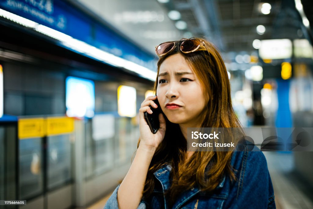 Displeased woman talking on smart phone Displeased woman talking on smart phone. Female is looking away while standing at subway station. She is with brown hair. 20-24 Years Stock Photo