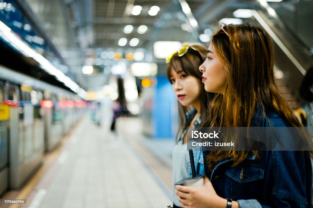 Female friends standing at subway station Female friends looking away while standing at subway station. Young women are waiting for train. They are on city break. 20-24 Years Stock Photo