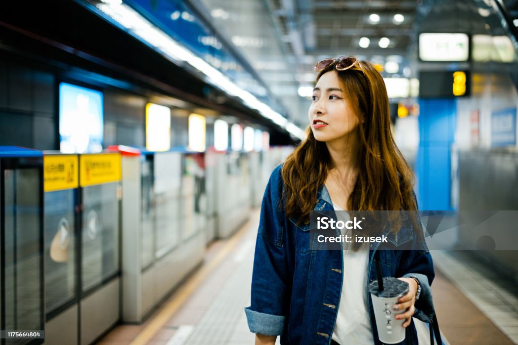 Female looking away while standing at subway station Female looking away while standing at subway station. Young woman with disposable cup is waiting for train. She is wearing denim jacket. Contemplation Stock Photo