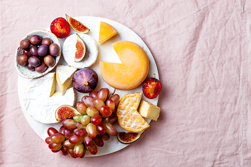 Appetizers, antipasti snacks. Cheese and fruit platter on marble board over pink linen tablecloth background. Top view, copy space