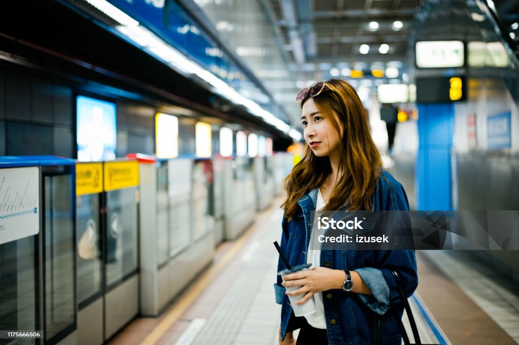 Thoughtful woman standing at subway station Thoughtful young woman looking away while standing at subway station. Female with disposable cup is waiting for train. She is wearing denim jacket. 20-24 Years Stock Photo