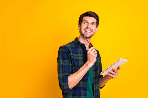 foto do indivíduo agradável com o organizador nas mãos que fazem notas que criam a idéia startup desgaste ocasional camisa checkered isolada fundo amarelo da cor - creativity thinking author inspiration - fotografias e filmes do acervo