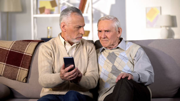 istock Elderly males holding smartphone sitting home sofa, online internet connection 1175671313