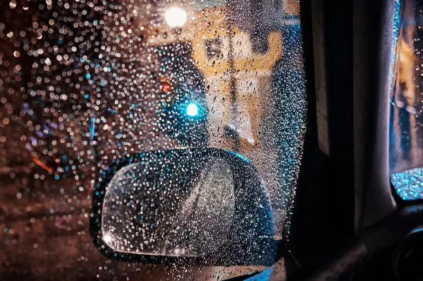Rearviewmirror of car close to a trafficlight whit the window full of raindrops