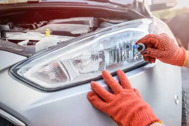 Photo of Mechanic holding lamp and cables from headlamp of car