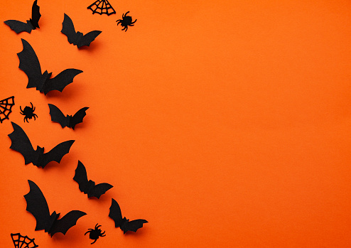 halloween  concept - black paper bats and decorations flying over orange background