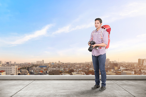Asian man with a backpack holding a camera to take pictures on the rooftop of the building