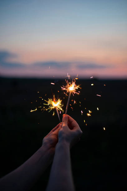 Female hands holding sparkling fireworks to the sky at twilight