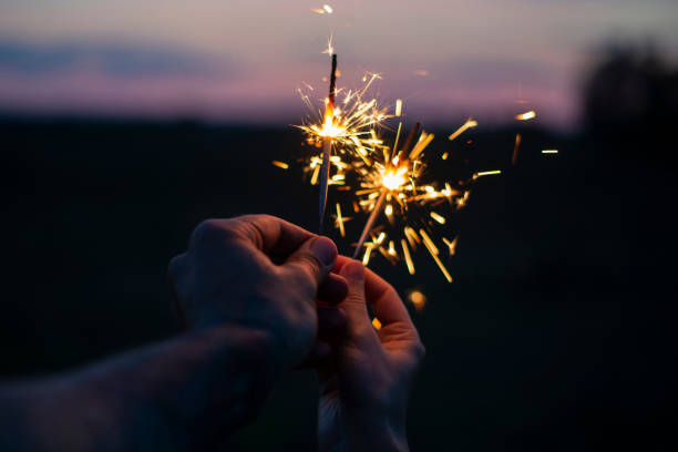 istock Two hands holding sparkling fireworks to the sky at twilight a 1175678933