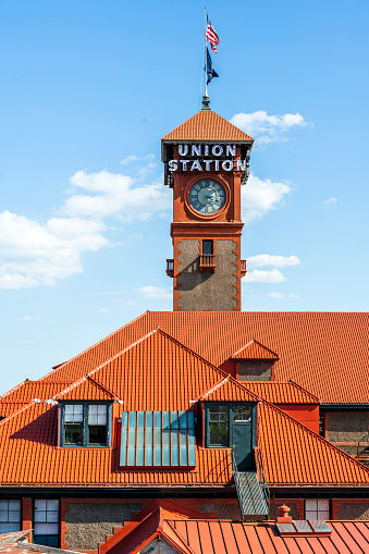Clock tower with flags and red tiled roof of the train station on a bright sunny day as a business card of old Portland and the peculiar architecture of the city