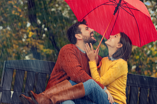 Cheerful embraced couple taking a walk on a rainy day at misty forest. Copy space.