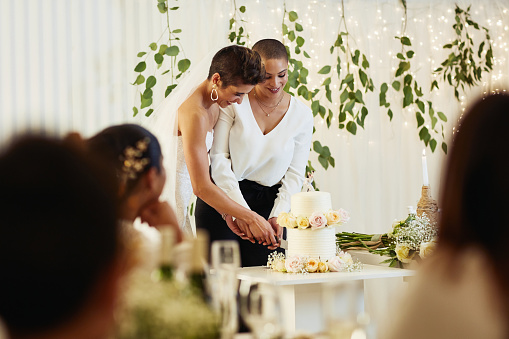 bride and groom together cut a wedding white cake and feed each other in a romantic setting.