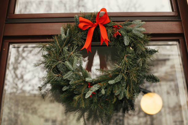 도시 거리의 휴일 시장에서 상점 앞에서 빨간 활과 열매가있는 세련된 크리스마스 화환. 텍스트의 공백입니다. 소박한 장식. 크리스마스 거리 장식입니다. - wreath christmas red bow 뉴스 사진 이미지