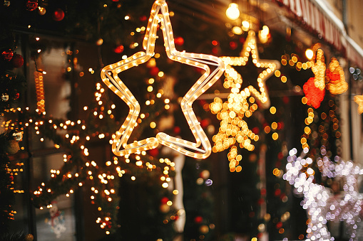Elegante iluminación de estrella dorada de navidad y ramas de abeto con bolas rojas y doradas, luces doradas bokeh en frente de la construcción en el mercado de vacaciones en la calle de la ciudad. Decoración callejera navideña photo