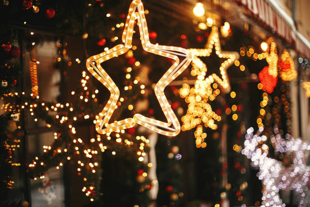 Stylish christmas golden star illumination and fir branches with red and gold baubles, golden lights bokeh on front of building at holiday market in city street. Christmas street decor stock photo