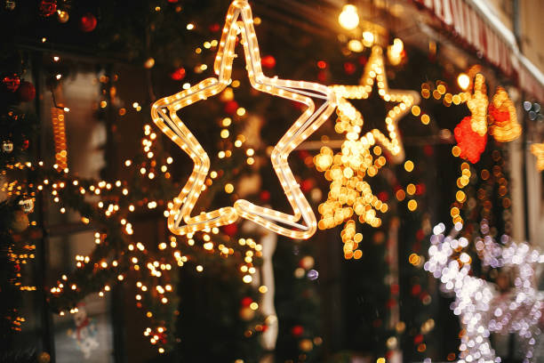 fotografii de stoc, fotografii și imagini scutite de redevențe cu iluminare elegantă a stelelor aurii de crăciun și ramuri de brad cu fleacuri roșii și aurii, lumini aurii bokeh în fața clădirii de la piața de vacanță de pe strada orașului. decorul străzii de crăciun - decoraţiune pentru locuinţă