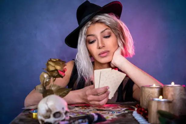Fortune teller reading Tarot cards and witch hat on table with candles and skull