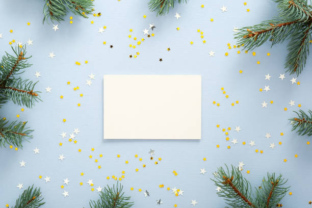 istock Blank paper greeting or invitation card on blue background with fir tree branches and glitter confetti stars. Christmas, New Year, winter holidays concept. 1175685183