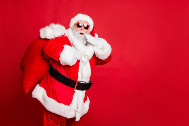 istock Photo of traditionally dressed amazed father hipster making noise while coming sneaking into house home at midnight noel holding hand near face large sack on back isolated vivid background copyspace 1175685826