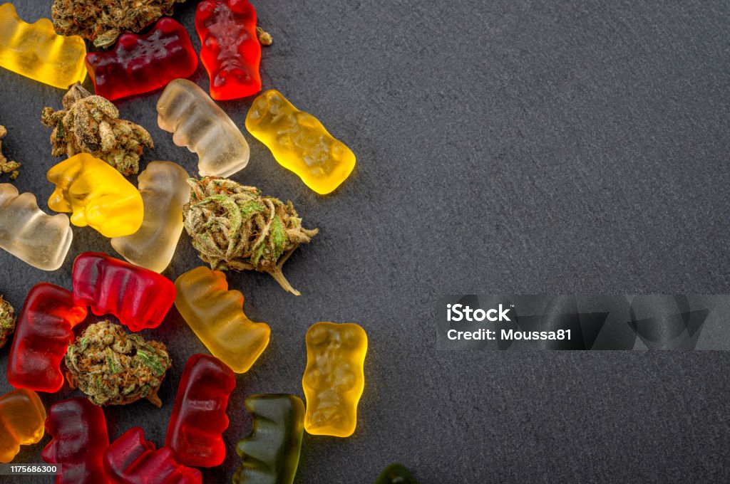 Cannabis edibles, medical marijuana, CBD infused gummies and edible pot concept theme with close up on colorful gummy bears and weed buds on dark background with copyspace Cannabis edibles, medical marijuana, CBD infused gummies and edible pot concept theme with close up on colorful gummy bears and weed buds on dark background with copy space Gummy Candy Stock Photo