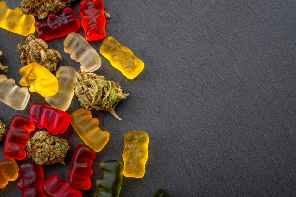 Cannabis edibles, medical marijuana, CBD infused gummies and edible pot concept theme with close up on colorful gummy bears and weed buds on dark background with copyspace Cannabis edibles, medical marijuana, CBD infused gummies and edible pot concept theme with close up on colorful gummy bears and weed buds on dark background with copy space cannabis gummy bears stock pictures, royalty-free photos & images