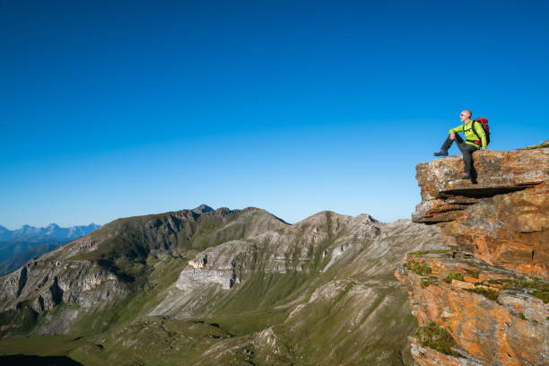 istock hiker sitting on mountain cliff peak in high alpine landscape with clear blue sky 1175687626