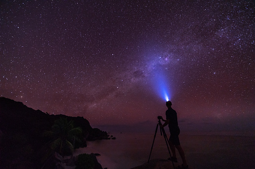 astro photographer on tropical island taking pictures of beautiful night sky with many stars and milky way