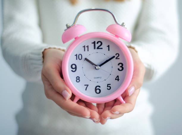 istock Woman holding alarm clock in hand 1175691188
