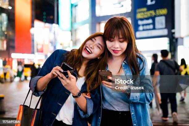 Cheerful Female Friends Using Smart Phone In City Stock Photo - Download Image Now - Asian and Indian Ethnicities, Friendship, Night