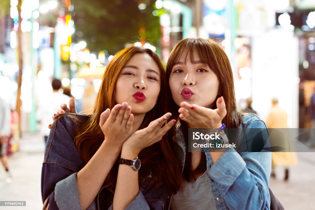 Female friends blowing kisses on city street Portrait of young friends blowing kisses on street. Beautiful women are spending leisure time in city. They are enjoying weekend together. Blowing a Kiss Stock Photo