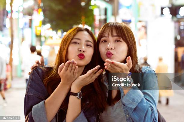 Female Friends Blowing Kisses On City Street Stock Photo - Download Image Now - Blowing a Kiss, Night, Human Lips