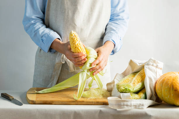 um avental fêmea do algodão do cozinheiro limpa o milho maduro na espiga. estilo natural rústico. o conceito de alimentos orgânicos. estilo kinfolk. - corn fruit vegetable corn on the cob - fotografias e filmes do acervo