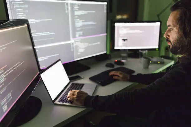 Computer programmer writing code in front of the monitors at late night.