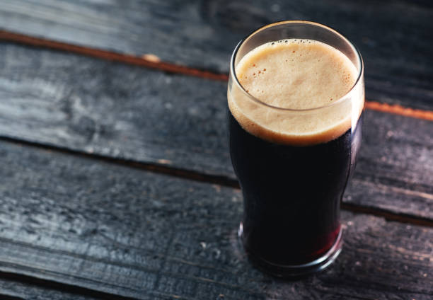 A glass of dark craft beer porter on a wooden table in a pub with copyspace A glass of dark craft beer porter on a wooden table in a pub with copyspace porter photos stock pictures, royalty-free photos & images