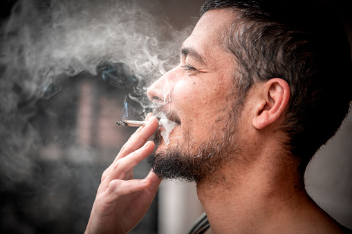 Bearded man smoking cigar against black brick wall close up
