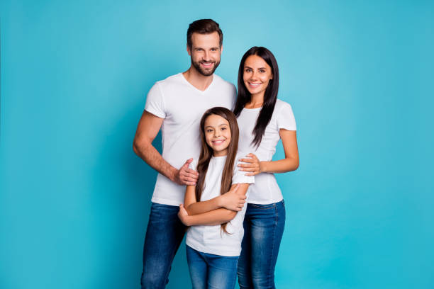 portrait of lovely family looking with toothy smile wearing white t-shirt denim jeans isolated over blue background - offspring child toothy smile beautiful imagens e fotografias de stock