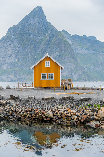 A yellow fishing cabin in Sakrisøy, a small fishing village in Moskenes Municipality on Lofoten islands in Nordland county, Norway with a mountain in background